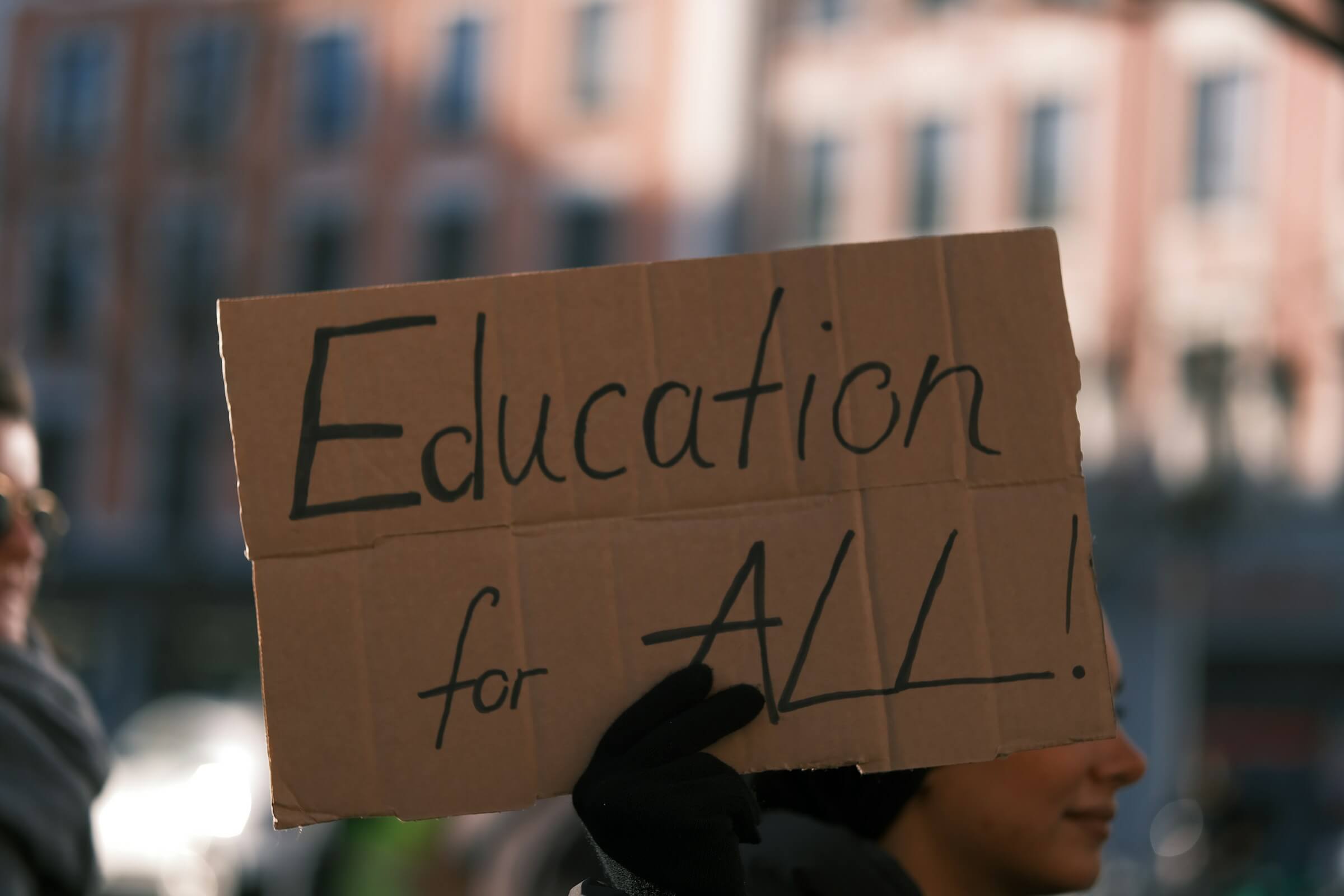 A person holding a cardboard sign that reads 'Education for ALL!' in bold, black letters, advocating for universal access to learning.