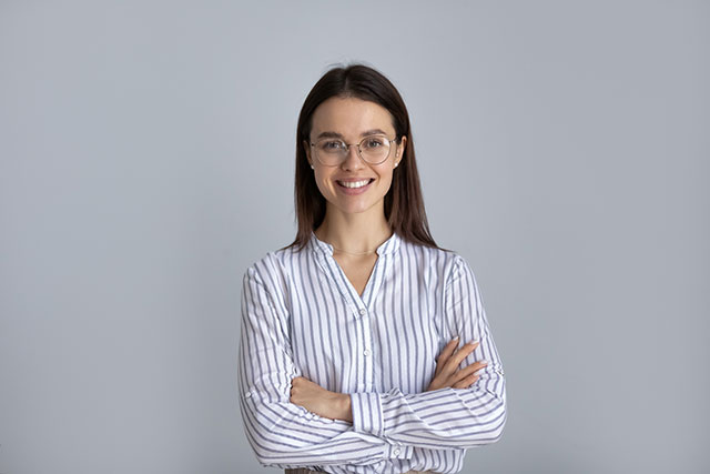 Confident young businesswoman in glasses and striped shirt, smiling with arms crossed, representing professional success and modern office wear.